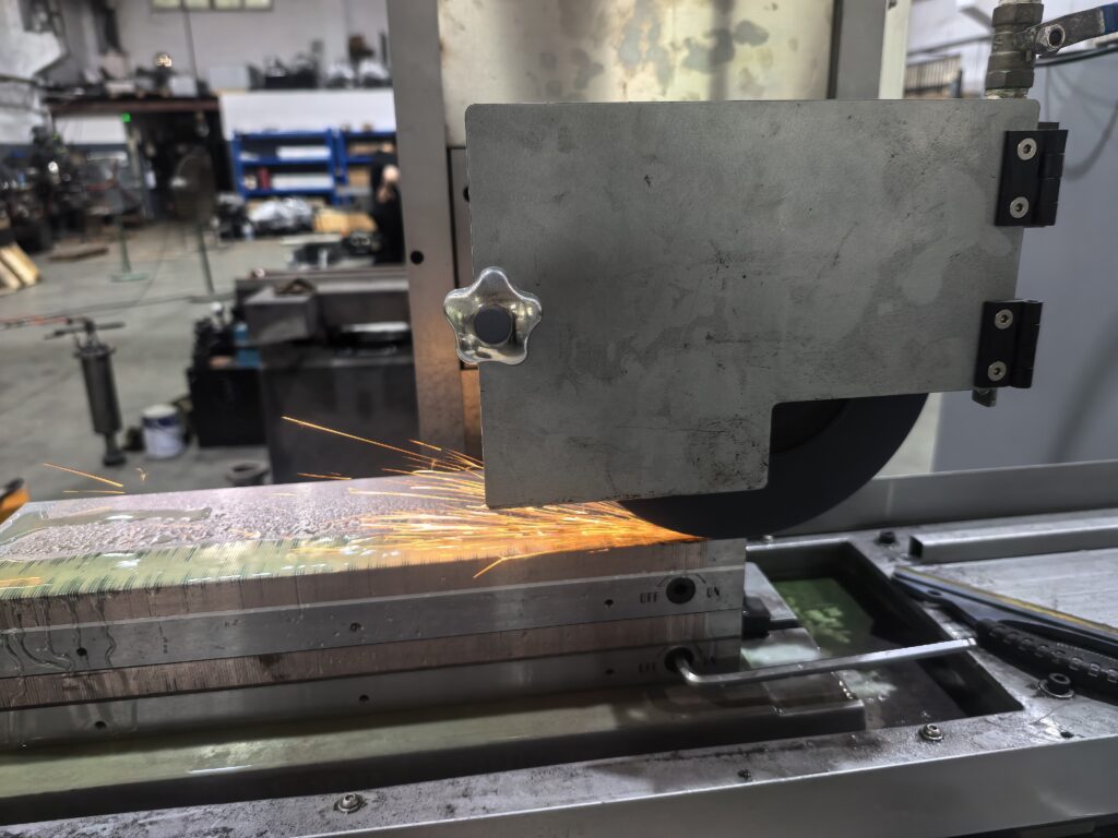 Surface grinder abrasive wheel grinding steel workpiece with coolant spray and sparks