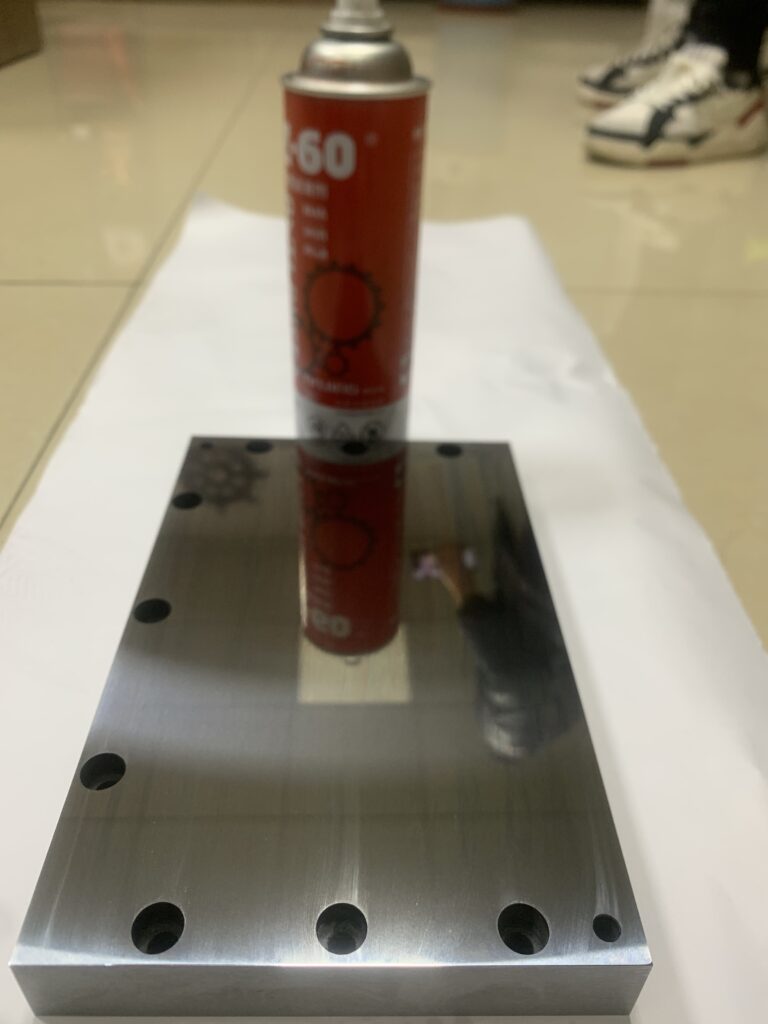 Mirror-like surface finish on an aerospace component ground by a high-precision surface grinder, reflecting workshop lights.